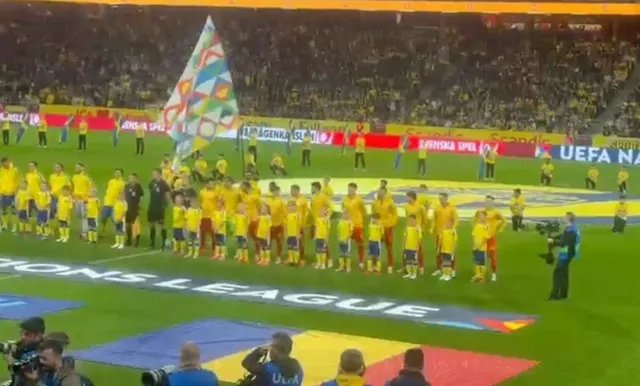 Jucători de fotbal îmbrăcați în echipamente galbene stau în linie pe un teren de fotbal verde în fața unor tribune pline de spectatori.