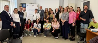 Un grup de oameni stă pozat într-o cameră cu pereți albi, purtând diverse haine casual și elegante.