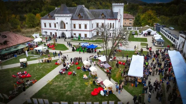 O vedere de sus a unei curți cu o clădire albă, corturi albe și colorate, oameni pe iarbă și alei pietruite.