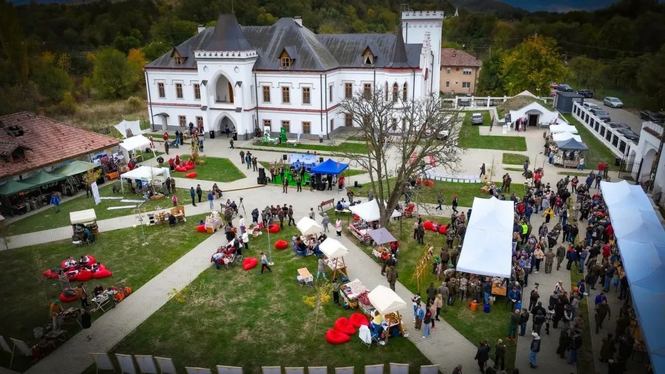 O vedere de sus a unei curți cu o clădire albă, corturi albe și colorate, oameni pe iarbă și alei pietruite.