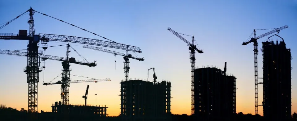 Siluete de macarale de construcții și clădiri în curs de edificare se ridică în fața unui cer la apus.