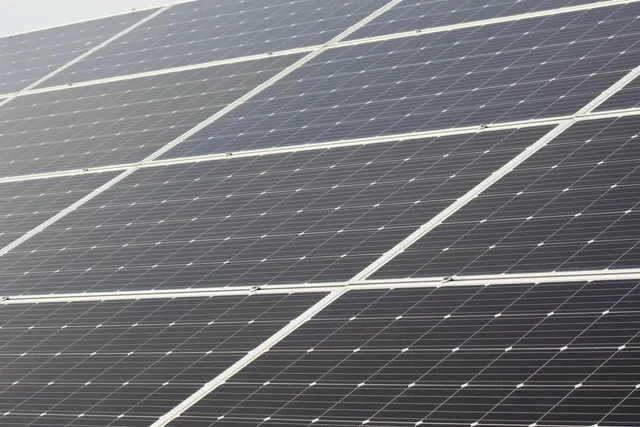 Mai multe panouri solare de culoare închisă sunt dispuse în rânduri paralele sub un unghi înclinat.