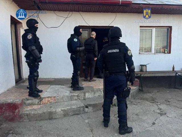Patru persoane în uniforme de poliție și jandarmerie stau în fața unei intrări de clădire lângă un bărbat cu pantaloni închiși.