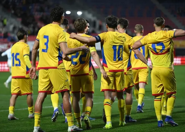 Un grup de fotbaliști în echipament galben cu detalii albastre și roșii stau întruniți pe un teren de fotbal sub luminile unui stadion.