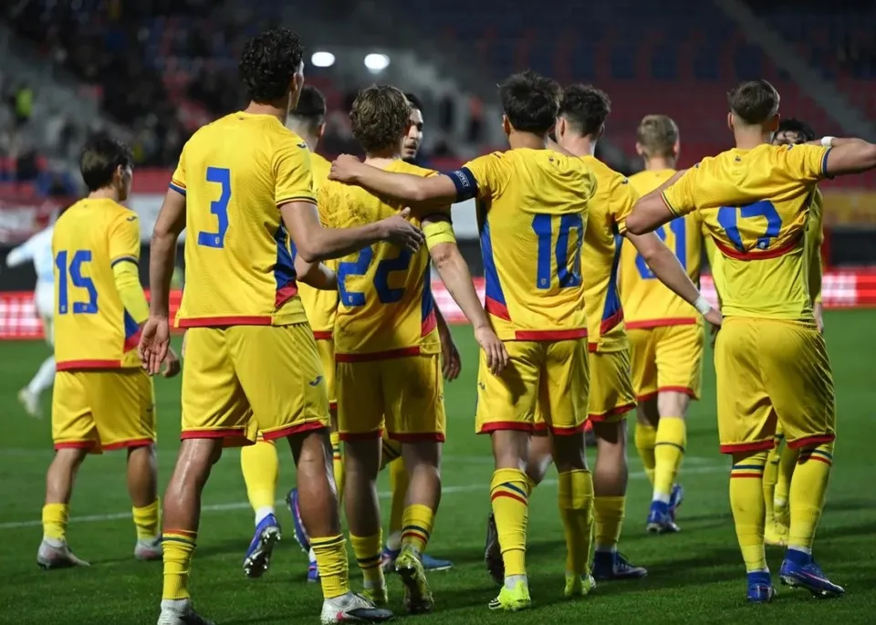 Un grup de fotbaliști în echipament galben cu detalii albastre și roșii stau întruniți pe un teren de fotbal sub luminile unui stadion.