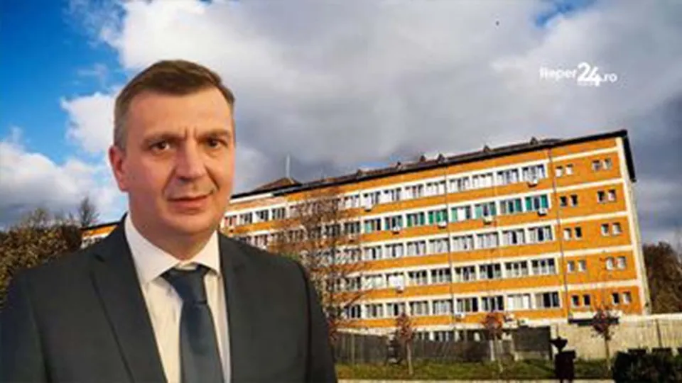 A man in a dark suit and blue tie stands in the foreground, with a large multi-story yellow and white building behind him under a cloudy sky.