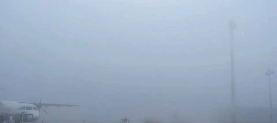 Un avion alb este parcat pe o pistă de aeroport într-un peisaj acoperit de ceață densă.