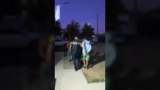 Un agent de poliție în uniformă întunecată conduce doi bărbați pe un trotuar în timpul serii.