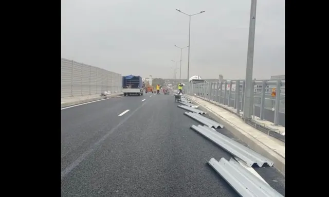 O porțiune de drum asfaltat cu bariere metalice de protecție pe marginea sa, un camion alb și stâlpi de iluminat sub un cer înnorat.