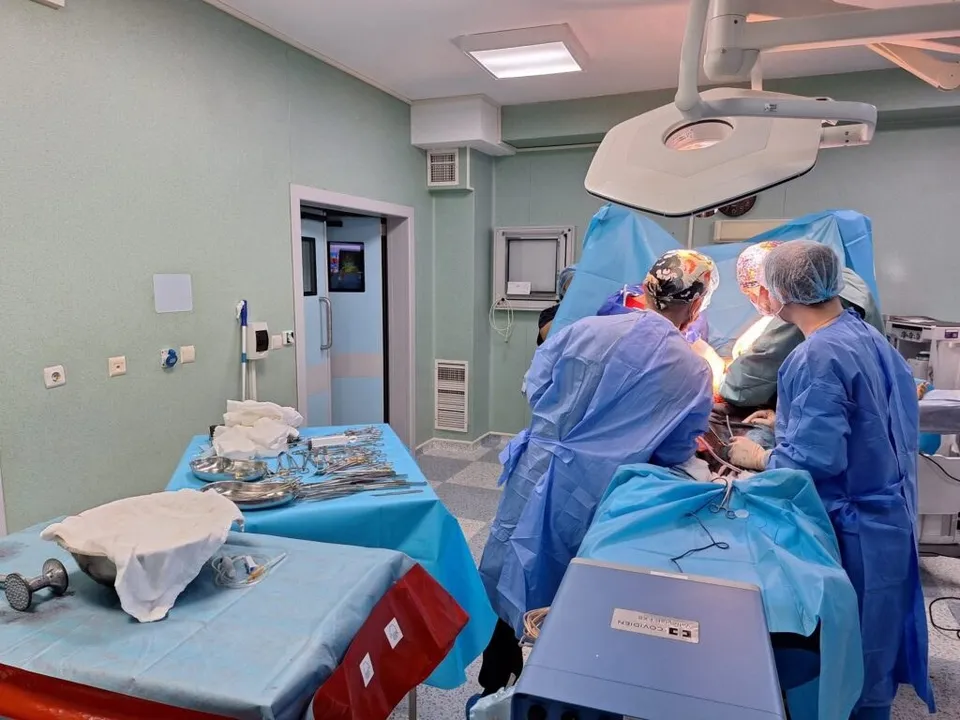 Echipe medicale în halate și mănuși sterile execută o procedură chirurgicală lângă un pacient acoperit în cadrul unei săli de operație.