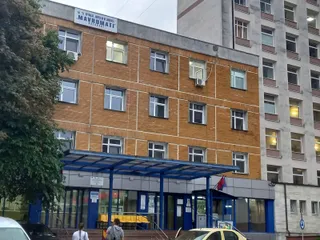 O clădire din cărămidă, cu copertină albastră, ferestre, copaci și câteva persoane în partea inferioară.