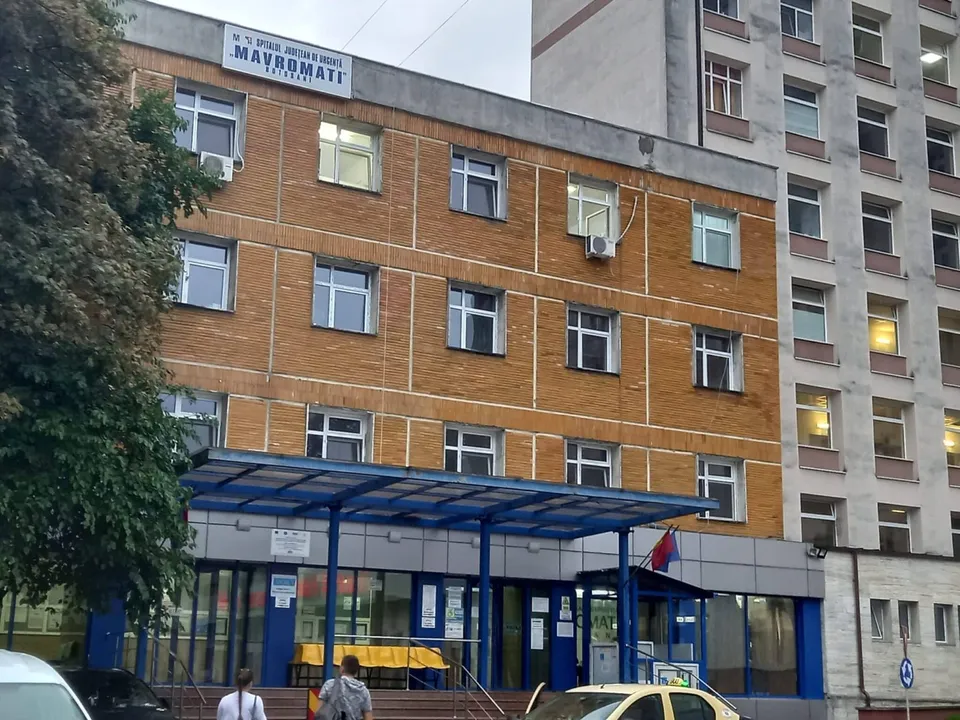 O clădire din cărămidă, cu copertină albastră, ferestre, copaci și câteva persoane în partea inferioară.