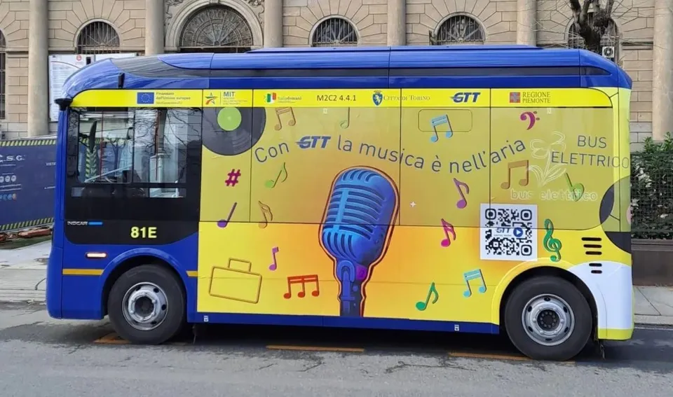 Un microbuz albastru și galben cu grafică muzicală este parcat pe un drum lângă o clădire cu arcade.