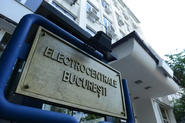Un semn metalic cu textul ELECTROCENTRALE BUCUREȘTI este montat pe un cadru albastru în fața unei clădiri albe cu unități de aer condiționat.