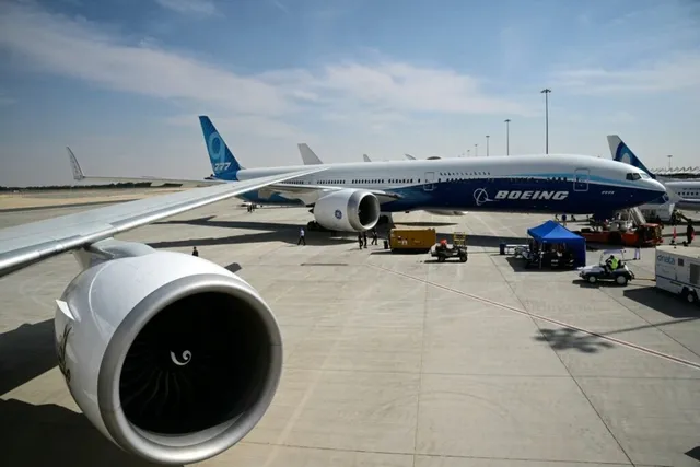 Un avion Boeing alb și albastru stă pe o pistă de aeroport lângă un motor de avion în prim-plan.