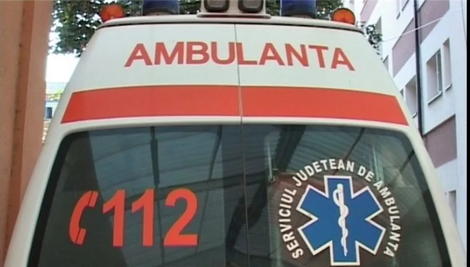 Partea din spate a unei ambulanțe albe prezintă inscripția AMBULANTA, numărul 112 și un simbol medical într-un cerc cu text.