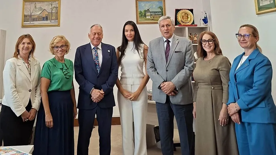 Șapte persoane stau în rând într-o încăpere cu tablouri pe perete și obiecte decorative pe rafturi.