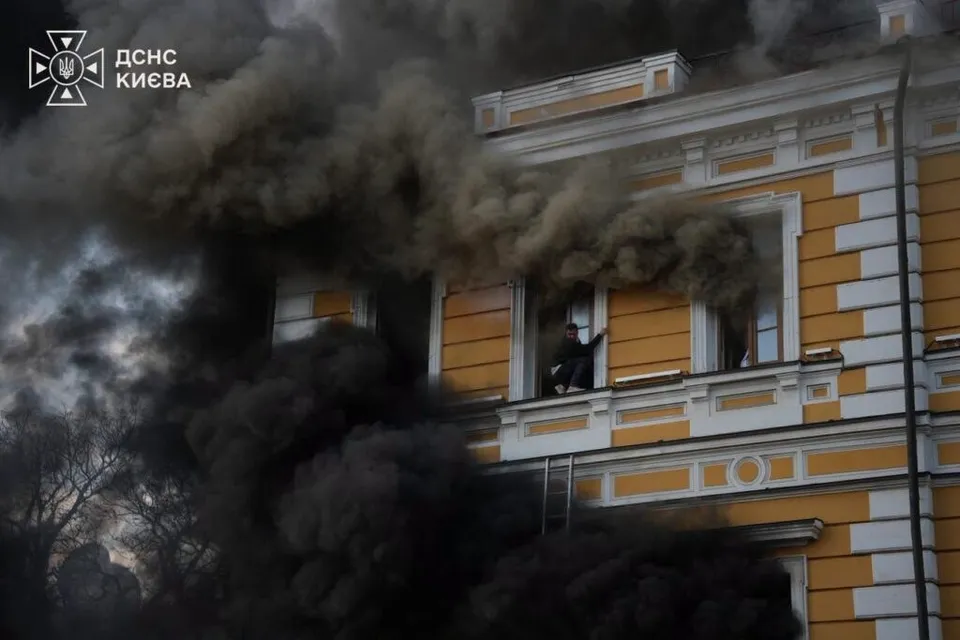 Fumoar dens și negru se ridică de la ferestrele unei clădiri galbene cu detalii albe sub un cer înnorat.