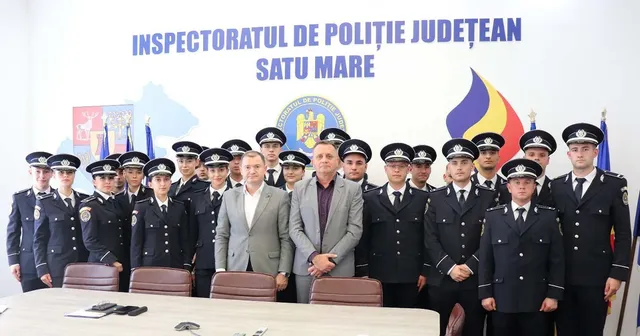 Un grup de persoane în uniforme de poliție și doi bărbați în haine civile stau în picioare în fața unui panou alb cu text albastru.