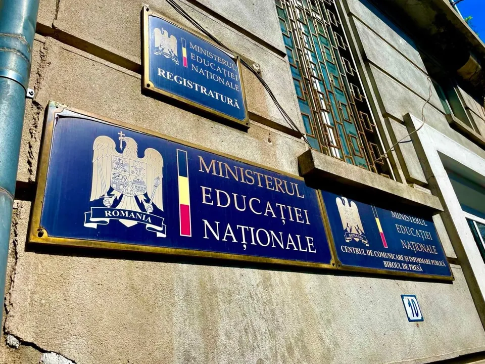 Plăcuțe albastre cu inscripții aurii și emblema României sunt montate pe o fațadă de clădire gri.