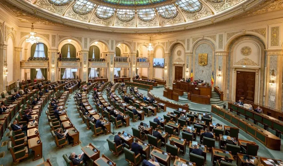 O cameră parlamentară circulară cu rânduri de birouri de lemn dispuse în semicercul, sub un plafon decorat cu ferestre rotunde și lustre.