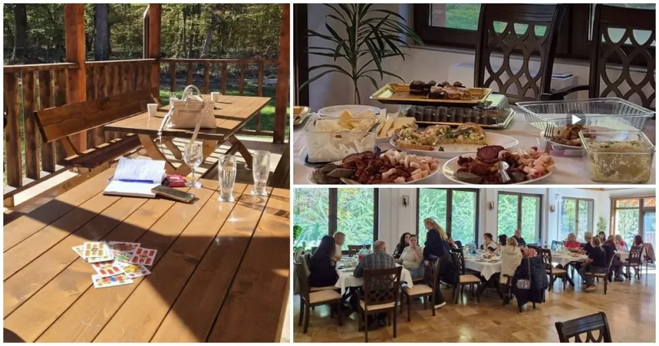 O masă de lemn cu pahare și obiecte, platouri cu mâncare și un grup de persoane așezate la mese într-o încăpere cu ferestre mari.