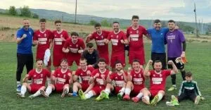 Un grup de fotbaliști în echipamente roșii și alții în echipamente albastre și mov pozează pe un teren de fotbal cu iarbă verde.