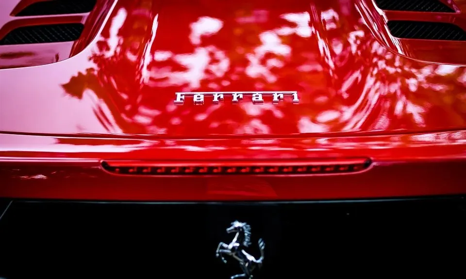 Un capot de mașină roșu strălucitor prezintă emblema Ferrari și un logo cu un cal în partea de jos.