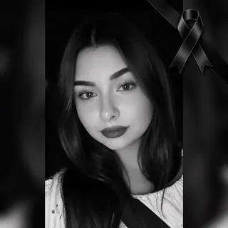 O femeie cu părul lung și întunecat privește spre cameră într-o fotografie de tip portret în alb și negru cu un fundal întunecat.