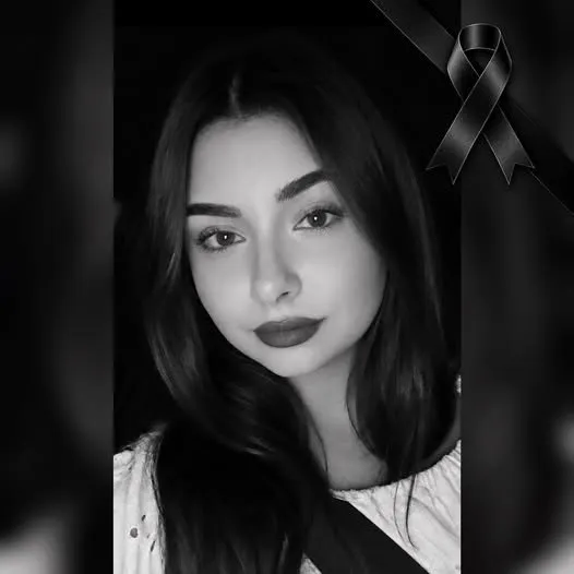 O femeie cu părul lung și întunecat privește spre cameră într-o fotografie de tip portret în alb și negru cu un fundal întunecat.