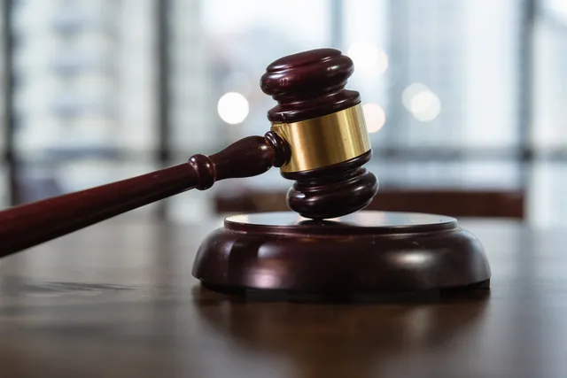 Un ciocan de judecător din lemn întins pe o masă de lemn din fața unui suport circular, cu un fundal difuz de ferestre.