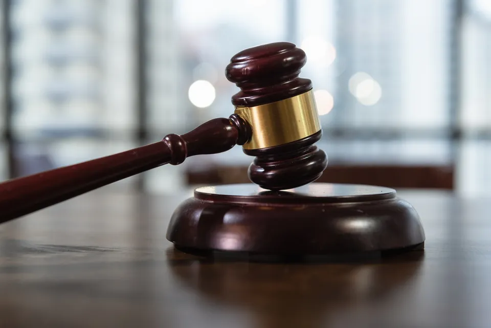 Un ciocan de judecător din lemn întins pe o masă de lemn din fața unui suport circular, cu un fundal difuz de ferestre.