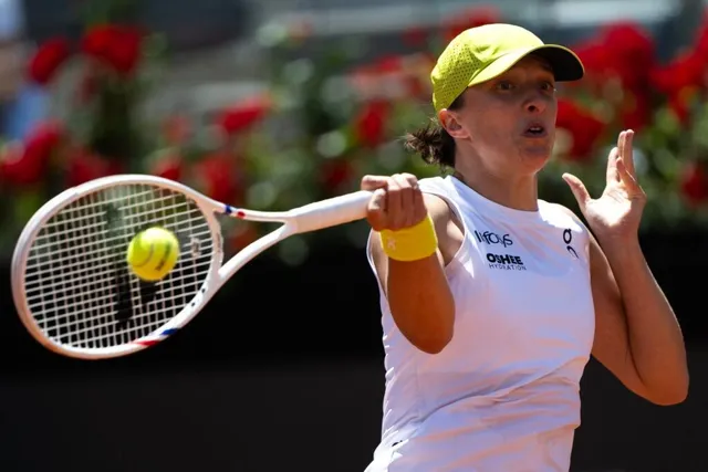 O femeie cu șapcă galbenă și tricou alb lovește o minge de tenis cu o rachetă pe un teren de joc.