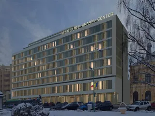 O clădire înaltă de hotel cu ferestre iluminate, situată lângă un drum cu mașini parcate și copaci fără frunze sub un cer închis.