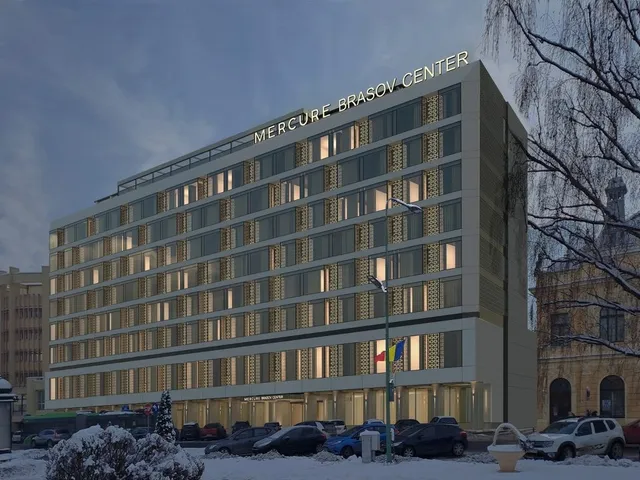 O clădire înaltă de hotel cu ferestre iluminate, situată lângă un drum cu mașini parcate și copaci fără frunze sub un cer închis.