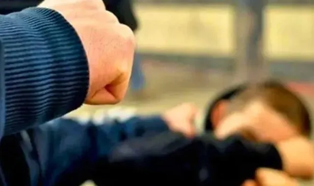 Un pumn închis este poziționat în prim-plan, în timp ce o persoană este întinsă pe un podea în fundalul neclar.