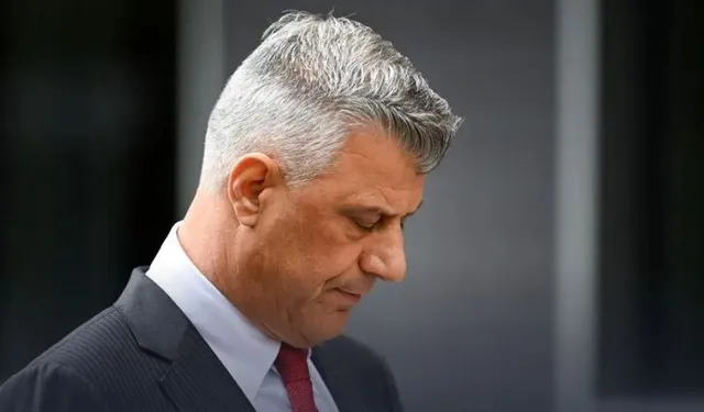 Un bărbat cu păr cărunt, îmbrăcat la costum cu cravată roșie, privește în jos, cu o expresie serioasă.