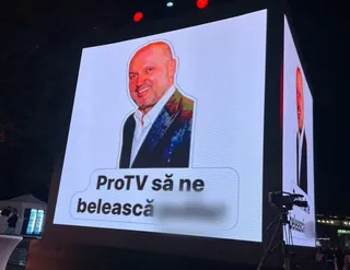 Un ecran mare afișează portretul unui bărbat cu sacou și un text pe fundal alb.