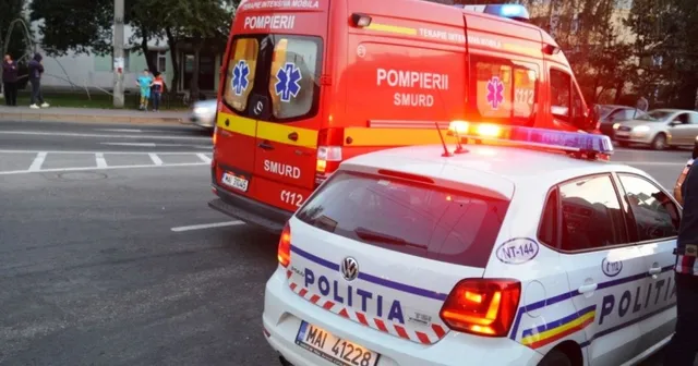 Un vehicul de poliție alb cu inscripții și o ambulanță roșie cu marcajul SMURD sunt parcate pe un drum asfaltat.