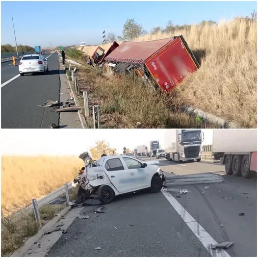 Un autoturism alb este oprit pe marginea drumului lângă un camion roșu răsturnat într-un taluz cu iarbă uscată.