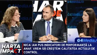 Un bărbat cu cravată purtată într-un costum închis la culoare stă la o masă între două femei în cadrul unui studio de televiziune.