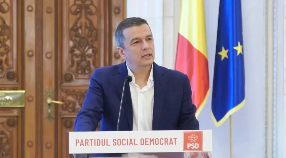 Un bărbat cu sacou albastru și cămașă albă stă în spatele unui pupitru marcat cu textul PARTIDUL SOCIAL DEMOCRAT și un logo roșu.