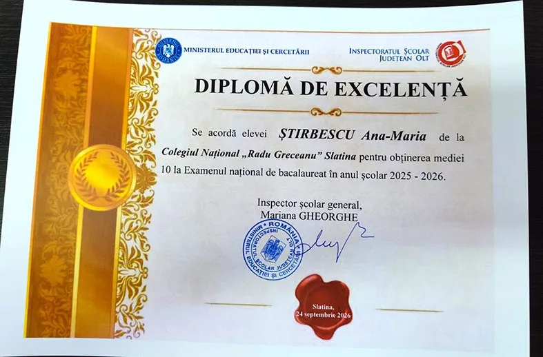 Un diplome de excelență cu text în limba română, sigilii și elemente decorative aurii este așezat pe o suprafață plană.