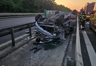 Un autoturism distrus stă întors pe o parte lângă bariera de protecție a unei autostrăzi, în prezența unor persoane cu echipament de protecție reflectorizant.