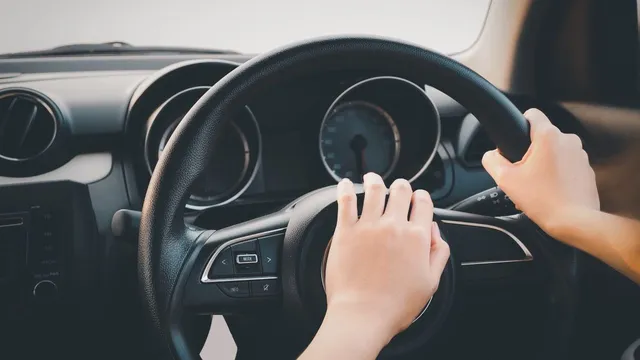 Două mâini de dimensiuni mici țin volanul unui autoturism în interiorul unei mașini.