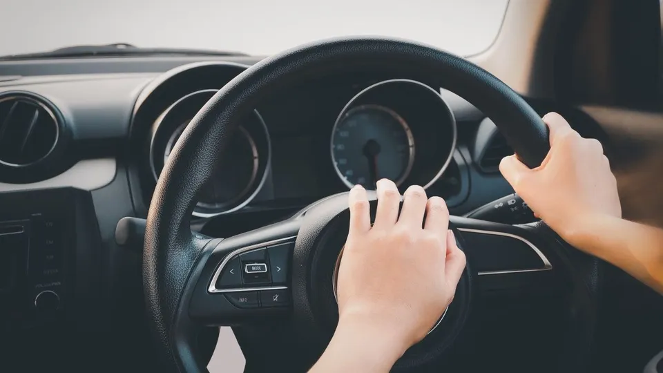 Două mâini de dimensiuni mici țin volanul unui autoturism în interiorul unei mașini.