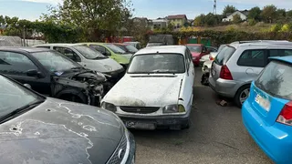 Mai multe mașini parțial deteriorate și murdare sunt parcate pe un teren asfaltat sub un cer senin.