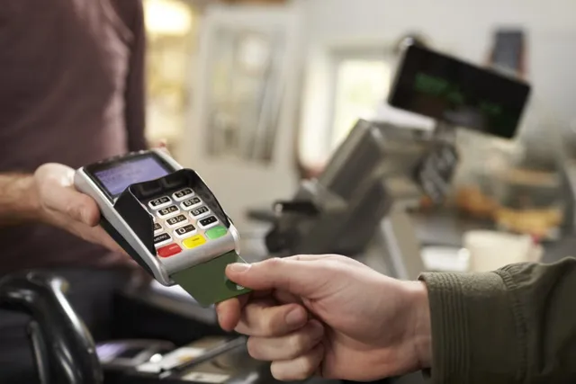 O persoană ține un card verde lângă un terminal de plată de culoare neagră și gri.