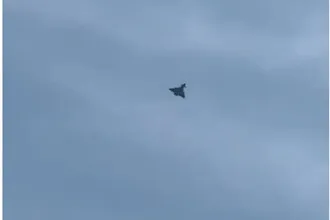 O siluetă întunecată de avion zboară pe un cer acoperit de nori gri.