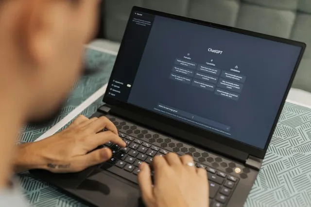 O persoană folosește un laptop deschis pe o masă, având mâinile poziționate pe tastatură.